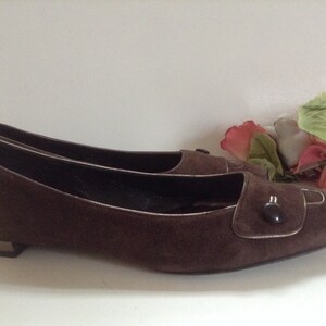 May include: Brown suede ballet flats with a button detail on the toe. The flats have a pointed toe and a low heel.