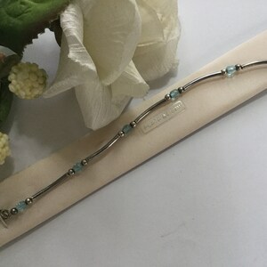 May include: A silver bracelet with light blue beads and a clasp. The bracelet is on a white background with the text "Flora & Joy" printed on it.