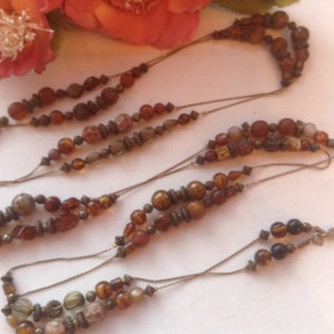 May include: A multi-strand necklace with brown, beige, and gold beads. The necklace is made of multiple layers of beads and string.
