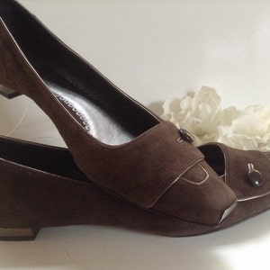 May include: A pair of brown suede heeled shoes with a pointed toe and a decorative button on the strap.