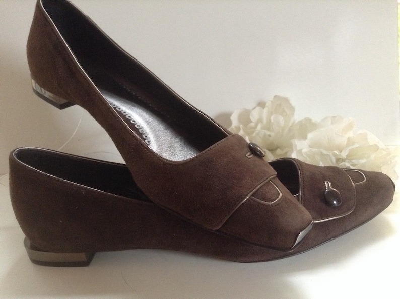 May include: A pair of brown suede heeled shoes with a pointed toe and a decorative button on the strap.