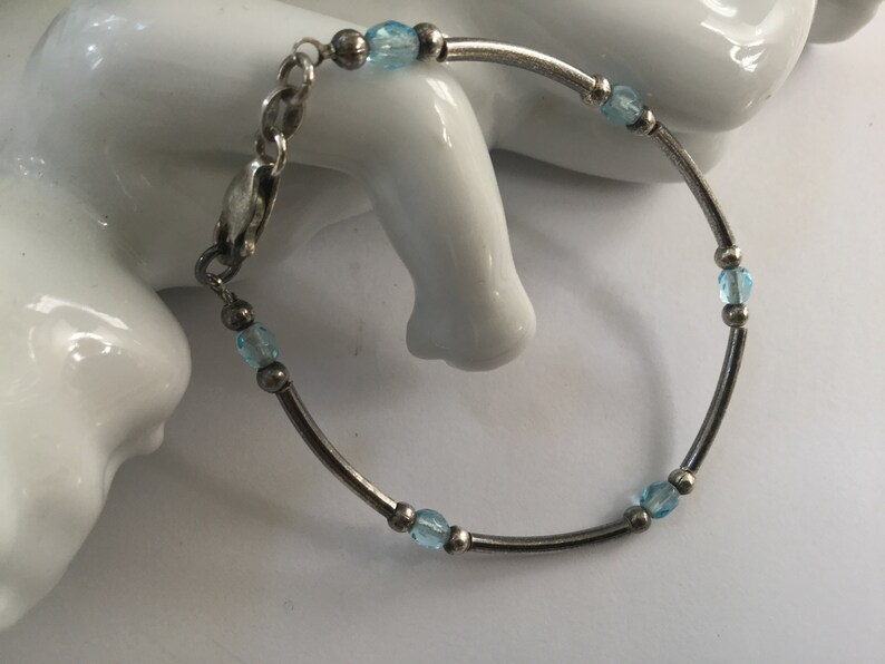 May include: A silver bracelet with a delicate chain and light blue beads.