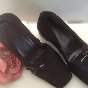 May include: A pair of black satin Valentino flats with a gold bow detail. The shoes have a pointed toe and a low heel.