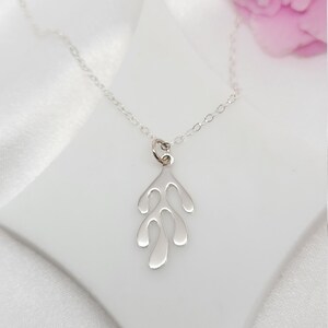 May include: A silver necklace with a delicate, abstract leaf-shaped pendant. The pendant is made of smooth, polished silver and has a slightly organic, flowing shape.