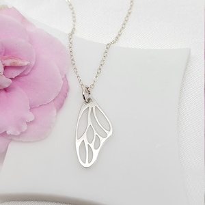 May include: A silver necklace with a delicate butterfly wing pendant. The pendant is cut out and has a detailed design.