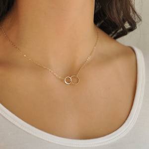 May include: A gold chain necklace with a delicate double circle pendant.