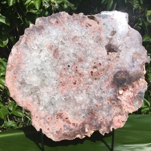 May include: A large, pink and white agate slice with a crystal-like texture. The agate is on a black metal stand.
