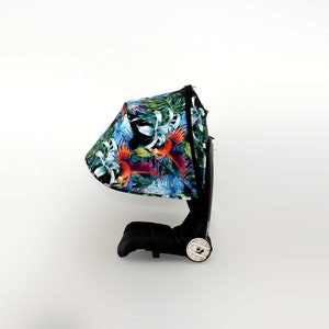 Könnte beinhalten: Ein schwarzer Kinderwagen mit einem tropischen Muster-Verdeck mit bunten Vögeln und grünen Blättern. Das Verdeck ist heruntergeklappt und der Kinderwagen steht auf weißem Hintergrund.