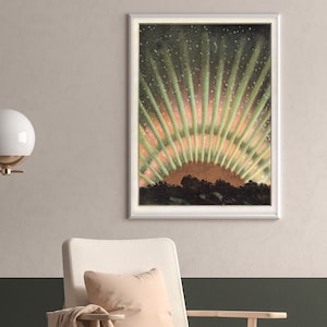 May include: Framed art print depicting a vibrant aurora borealis. The artwork features a dark foreground with a mountain range silhouette, and a colorful display of green and orange light radiating upwards. The print is in a white frame.