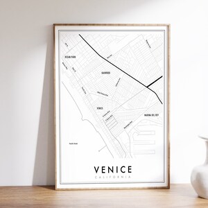 May include: A black and white map print of Venice, California. The map shows the streets and neighborhoods of Venice, including Ocean Park, Oakwood, and Marina del Rey. The text "Venice, California" is printed at the bottom of the map.