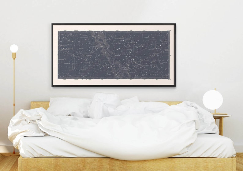 Puede incluir: Un mapa en blanco y negro de las constelaciones enmarcado colgado sobre una cama blanca con ropa de cama blanca. El mapa est&aacute; sobre un fondo azul oscuro con estrellas blancas y nombres de constelaciones.