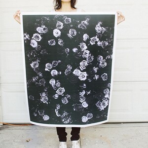 May include: A woman holds a large black and white print of a floral pattern. The print features white roses on a black background.