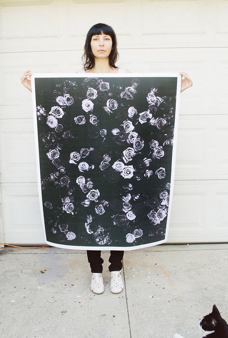 May include: A woman holds a large black and white print of a floral pattern. The print features white roses on a black background.