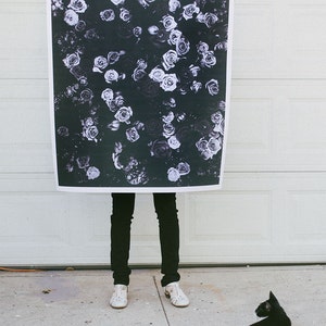 May include: A black and white print of a floral pattern featuring many roses. The print is being held up by a person in front of a white garage door.