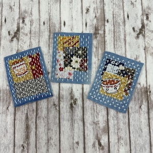 May include: Three small, square, denim patches with hand-stitched white thread. Each patch features a different design: a ramen bowl, a package of noodles, and a floral pattern. The patches are arranged on a light wood-grain surface.