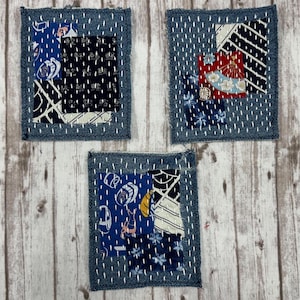 May include: Three rectangular denim fabric patches featuring white sashiko-style running stitches. Each patch is decorated with various blue, black, white, and red patterned fabric scraps layered on top, showcasing diverse geometric and floral motifs.