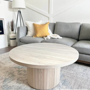 May include: A round, light-colored wooden coffee table with a cylindrical base made of vertical wooden slats. The table sits on a patterned rug in a living room setting. The text "STRAIGHT PATTERN" is visible on the image.