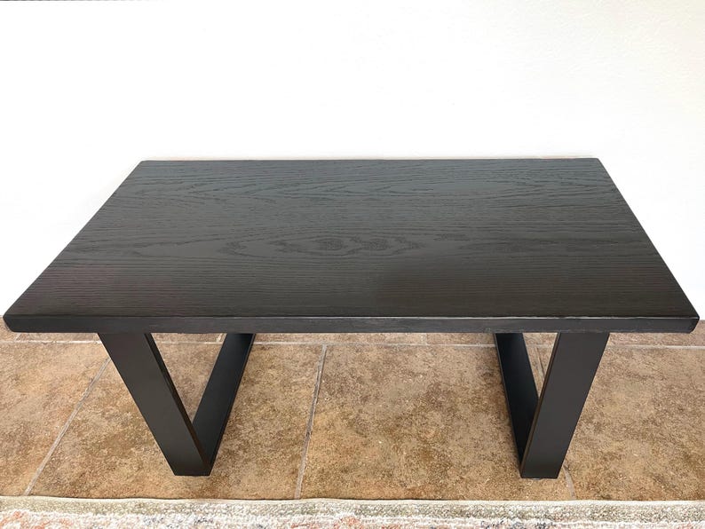 May include: A rectangular black wooden table with a dark finish. The table has a simple design with V-shaped legs. The table is approximately 48 inches long and 24 inches wide, suitable for various home decor styles.
