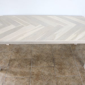 White oak wood table shown with square wood legs. Rectangle shape top. Herringbone pattern on the top of table.