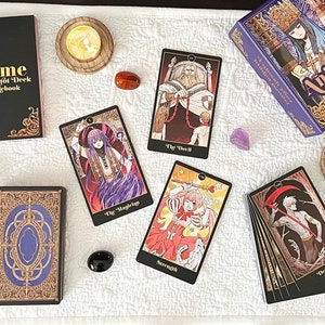 May include: An assortment of tarot cards, a guidebook, and a box set, all with an anime theme, are arranged on a white cloth. The cards feature colorful illustrations. Candles, crystals, and other mystical items surround the tarot set.