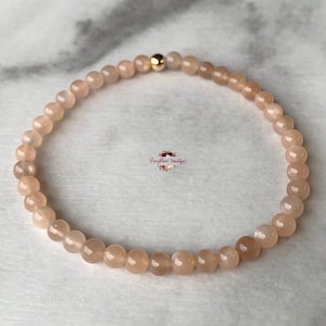 May include: A delicate bracelet made with small, light peach-colored beads. The bracelet has a gold clasp.