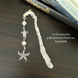 Könnte beinhalten: Silbernes Lesezeichen mit einem Delfin-Design und einem Anhänger mit einem Seestern, einer Schildkröte und Perlen. Das Lesezeichen liegt auf einer Holzoberfläche mit Büchern im Hintergrund. Der Text "70 Gemstones 4 Bookmark Patterns Available" ist sichtbar.