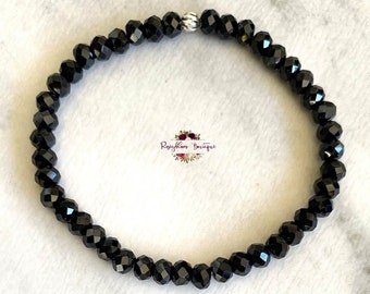 May include: A black beaded bracelet with a silver clasp. The beads are faceted and have a shiny finish.