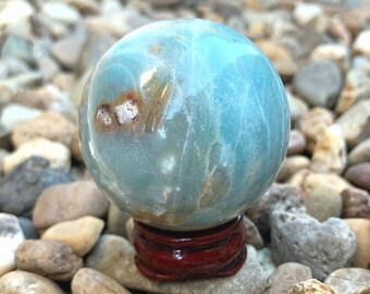Puede incluir: Una esfera de ágata azul y blanca sobre un soporte de madera. La esfera tiene un patrón de remolino y está pulida a un acabado liso.