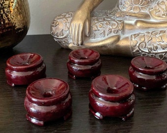 May include: Four dark red wooden display stands for crystals or other small objects. The stands are round and have a raised center. They are arranged on a dark wood surface in front of a gold statue of Buddha.