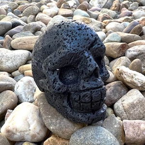 Op de afbeelding: Zwarte schedel sculptuur gemaakt van lavasteen met een getextureerd oppervlak. De schedel heeft een piratenooglap en een tandenrij.