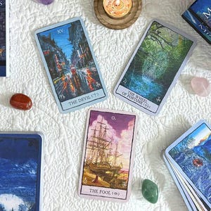 May include: An overhead shot of a Mindscapes Tarot deck and several tarot cards, arranged on a white quilted surface. The deck is blue with the title "Mindscapes Tarot" and the author's name. The cards feature colorful landscape art, candles, and crystals.