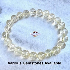 May include: A bracelet made of clear, faceted gemstone beads. The beads are strung on a clear elastic cord. The bracelet is on a white surface. Various Gemstones Available.
