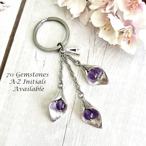 May include: Silver charm keychain with three purple gemstone flowers. The charm is attached to a silver key ring. The text "70 Gemstones A-Z Initials Available" is visible in the image.