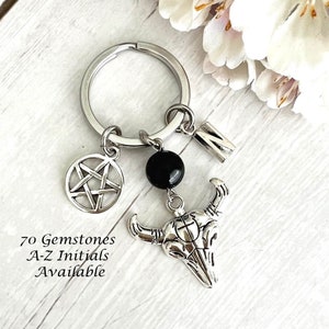 May include: Silver keychain with a black gemstone, a pentagram charm, a bull skull charm, and a letter "M" charm. 70 Gemstones A-Z Initials Available.