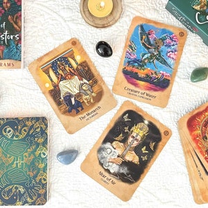May include: An arrangement of oracle cards, crystals, candles, and books. The cards are titled "Secrets of the Ancestors" and feature colorful illustrations. Other items include a selenite wand, a clear crystal ball, and a small abalone shell.