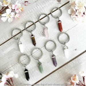 May include: A set of eight keychains featuring different colored gemstone point charms. Each keychain has a silver key ring and a silver charm with a gemstone point. The gemstones include amethyst, rose quartz, tiger's eye, clear quartz, black obsidian, green aventurine, red jasper, and white quartz.