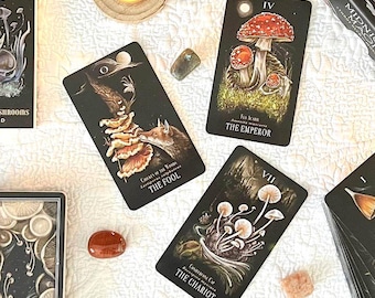 May include: A collection of tarot cards, crystals, candles, and books arranged on a white cloth. The tarot cards feature illustrations of mushrooms and other mystical imagery. The words "Midnight Magic" are visible on the card boxes.