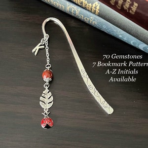 May include: Silver bookmark with a red gemstone, a silver leaf charm, and a red ladybug charm. The bookmark has a floral design and the text "70 Gemstones 7 Bookmark Patterns A-Z Initials Available".