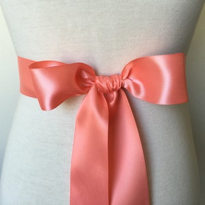 May include: A coral satin ribbon tied in a bow around a white mannequin.