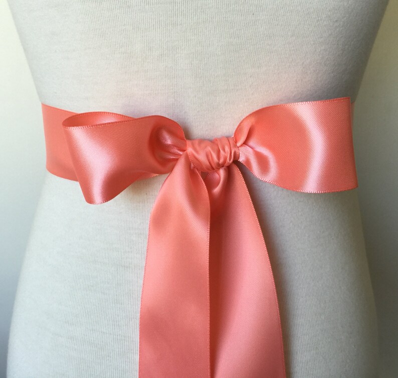 May include: A coral satin ribbon tied in a bow around a white mannequin.