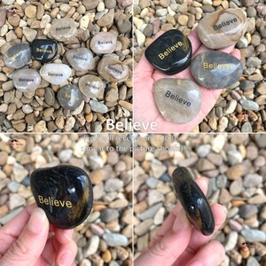 May include: A collection of smooth, gray and black stones with the word "Believe" written in gold lettering. You will receive one stone similar to the picture shown.