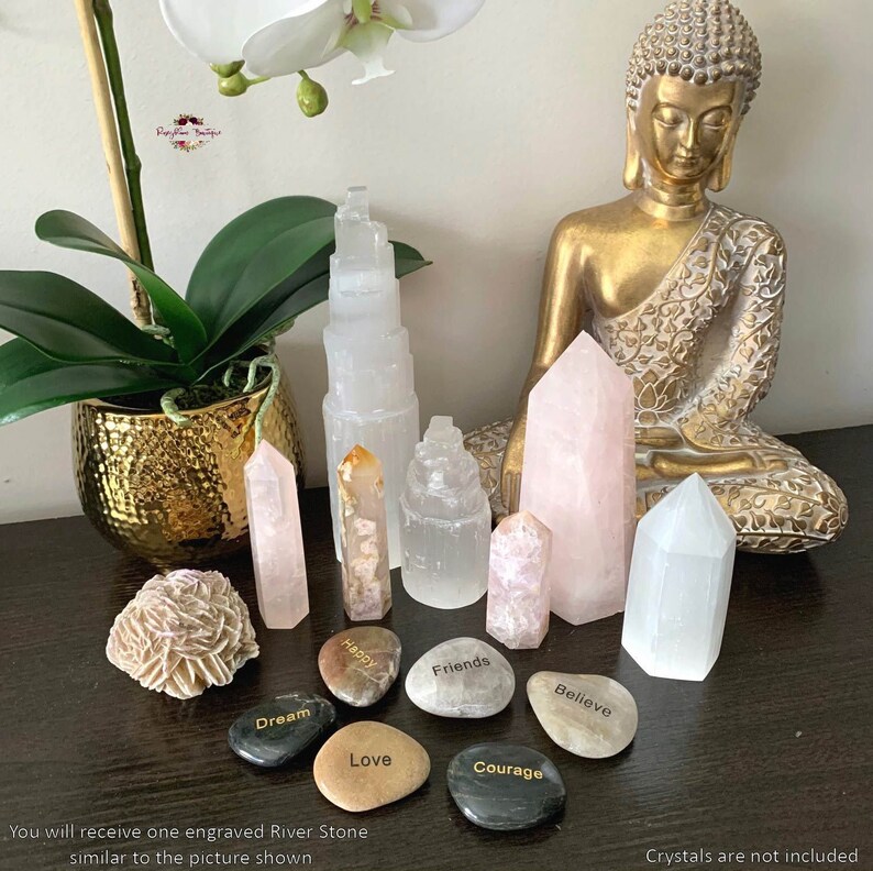 May include: A collection of white selenite crystals, including a selenite tower, selenite points, and a selenite wand. There are also several engraved river stones with words like "Dream", "Happy", "Friends", "Love", "Courage", and "Believe". A golden Buddha statue sits in the background.