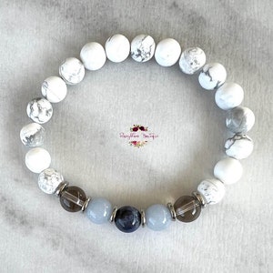 May include: White howlite beaded bracelet with a dark blue sodalite, light blue aquamarine, and smoky quartz beads. The bracelet is accented with silver spacers.