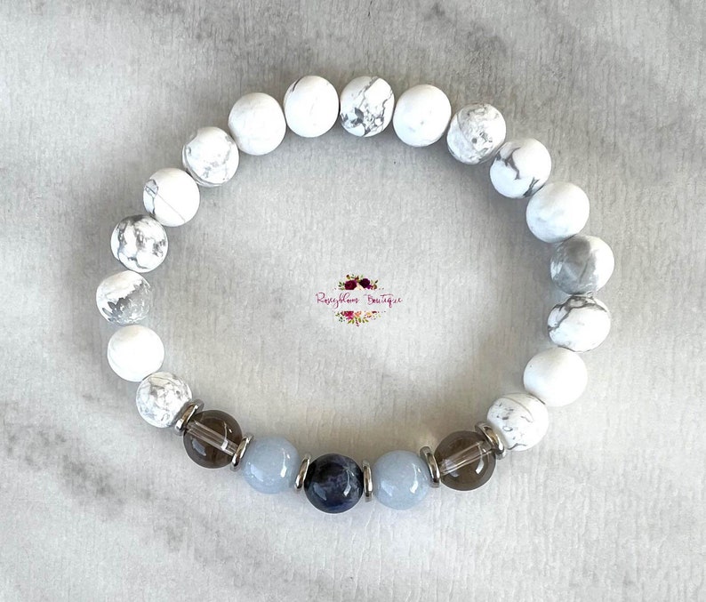 May include: White howlite beaded bracelet with a dark blue sodalite, light blue aquamarine, and smoky quartz beads. The bracelet is accented with silver spacers.