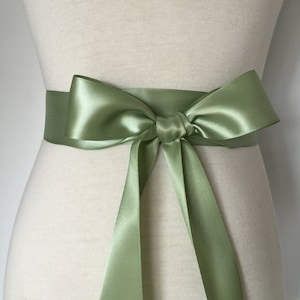 May include: A sage green satin ribbon tied in a bow around a waist. The ribbon is about 2 inches wide.