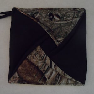 Może przedstawiać: Kwadratowy uchwyt do garnków z czarnym wykończeniem i wzorem kamuflażu. Uchwyt do garnków ma pętlę do zawieszania i ma chronić dłonie przed gorącem podczas obchodzenia się z gorącymi naczyniami.