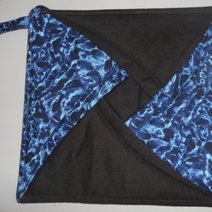 May include: Square quilted potholder with a black and blue water pattern design. The potholder has a loop for hanging and is made of fabric. The blue pattern has white accents.