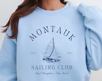 May include: Light blue sweatshirt with a navy blue graphic of a sailboat and the text "Montauk Sailing Club Est. 1900 East Hampton, New York"