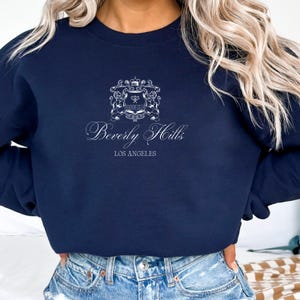 May include: A navy blue sweatshirt with a white graphic of a crest with a tennis racket and the text "Beverly Hills Los Angeles".