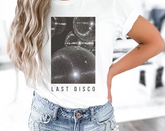 May include: White t-shirt with a rectangular graphic featuring multiple disco balls. The graphic is in black and white. The words "LAST DISCO" are printed in black below the graphic. The shirt is paired with denim shorts.